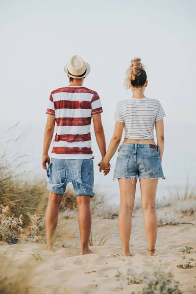 Back view of young couple holding hands and looking on sea