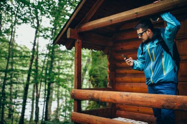 Genç adam akıllı telefon ayakta ahşap orman evde kullanma