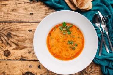 ahşap masa üzerinde lezzetli domates çorbası, ekmek ve çatal ile beyaz plaka üst görünümü