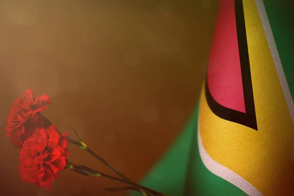 De vlag van Guyana voor eer van veteranen of memorial day met twee rode carnation bloemen. Glorie aan Guyana helden van oorlog concept op oranje donkere fluweel. — Stockfoto