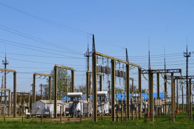 Mavi gökyüzünde yüksek voltajlı elektrik hatları ve gerilim transformatör blokları. Elektrik güç trafomerkezi
