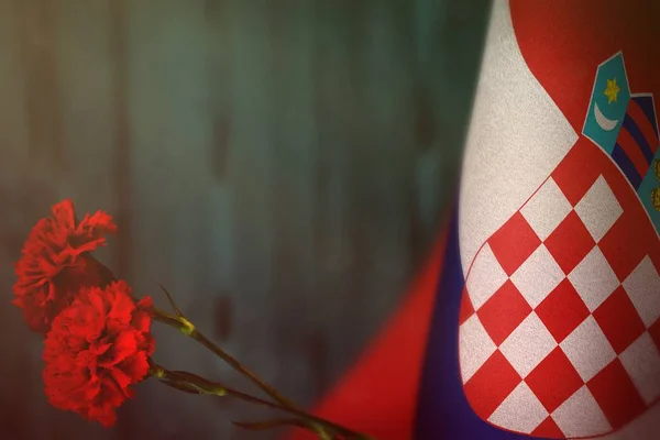 Bandera de Croacia por el honor del día de los veteranos o el día conmemorativo con dos flores rojas de clavel. Gloria a los héroes croatas del concepto de guerra en la pared de madera natural borrosa azul claro. antecedentes . —  Fotos de Stock