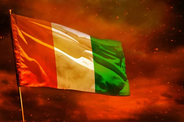 Bandera ondeando Cote d Ivoire en el cielo rojo carmesí con el fondo de pilares de humo. Concepto de problemas . —  Fotos de Stock