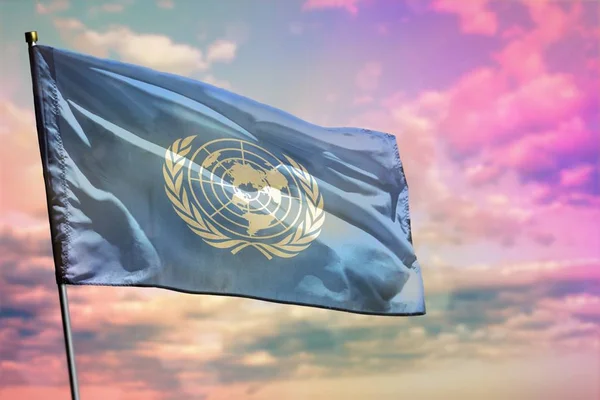 Ondeando la bandera de las Naciones Unidas sobre un colorido fondo nublado. Concepto de prosperidad . — Foto de Stock