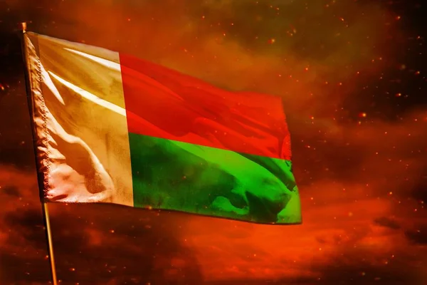 Flambant drapeau malgache sur ciel rouge cramoisi avec des piliers de fumée arrière-plan. Concept de troubles . — Photo