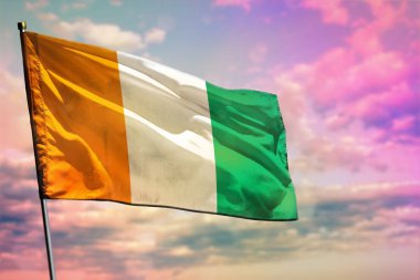 Renkli bulutlu gökyüzü arka plan üzerinde Fluttering Cote d Ivoire bayrağı. Refah kavramı.