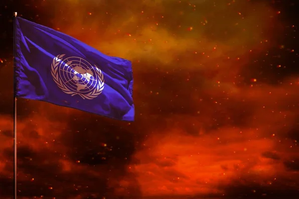 Fluttering United Nations flag mockup with blank space for your data on crimson red sky with smoke pillars background. United Nations problems concept.