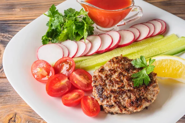 Kıyılmış biftek pirzola turp kiraz domates dilim salatalık maydanoz limon ve sosu ketçap kavramı gıda yaz ev yapımı piknik Barbekü assorty karışımı sebze ile beyaz tabakta ızgarada pişmiş.