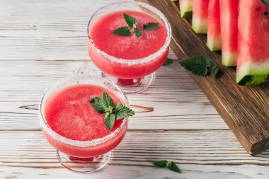 İçki smoothies cam yemeklerinde kırmızı karpuz gelen beyaz şeker dekore edilmiş ve kesme tahtası beyaz masa kavramına sağlıklı beslenme diyet detoks meyve parçaları nane yaprakları.