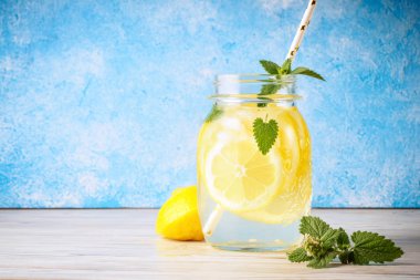 Doğal limon su ev yapımı yiyecek soda İçecek meyve dilimleri ve saman içme popüler detoks antioksidan infüzyon bardak içecektir ahşap masa mavi arka plan kokteyl kavanoz limonata nane yaprakları.