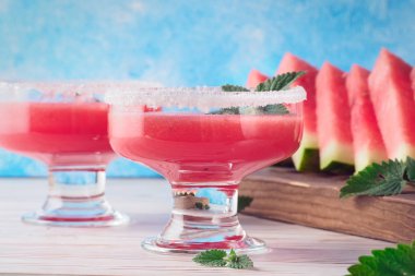 İçki smoothies cam yemeklerinde kırmızı karpuz gelen beyaz şeker dekore edilmiş ve nane meyve parçaları kesme tahtası beyaz masa ve mavi arka plan kavramı sağlıklı beslenme diyet detoks üzerinde bırakır..