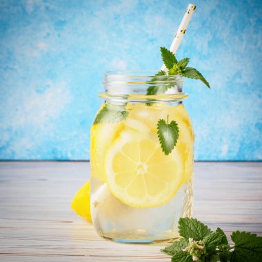 Doğal limon su ev yapımı yiyecek soda İçecek meyve dilimleri ve saman içme popüler detoks antioksidan infüzyon bardak içecektir ahşap masa mavi arka plan kokteyl kavanoz limonata nane yaprakları.