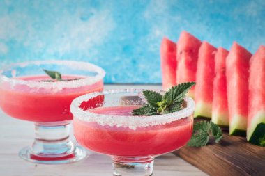 İçki smoothies cam yemeklerinde kırmızı karpuz gelen beyaz şeker dekore edilmiş ve nane meyve parçaları kesme tahtası beyaz masa ve mavi arka plan kavramı sağlıklı beslenme diyet detoks üzerinde bırakır..