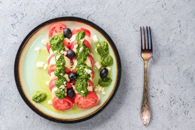 Domates ve mozzarella caprese salatası ve pesto sos ile zeytin gri masada