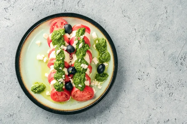 Tomaten-Mozzarella-Caprese-Salat und Pesto-Sauce mit Oliven auf grauem Tisch lizenzfreie Stockfotos