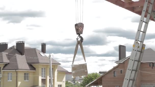 Grue levant charge contre ciel nuageux au sommet de la construction. Bôme de grue de construction avec crochet en acier. — Video