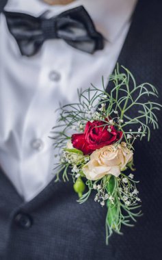 şık lüks beyaz papyon ve beyaz kırmızı çiçekler ile mavi elbiseli Genç Sevimli damat. güzel düğün yaka çiçeği damat için