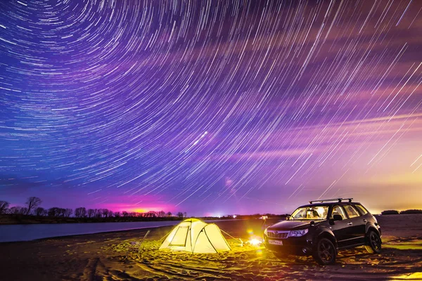 NIKOLAEVKA, RUSKO - 03. KVĚTEN 2019: Noční kempování u řeky. Hvězdné stezky na obloze. Subaru Forester stojí u stanu — Stock fotografie