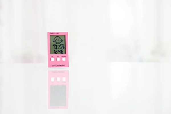 Rosa elektronisches Hygrometer auf weißem Tisch vor dem Fenster — Stockfoto