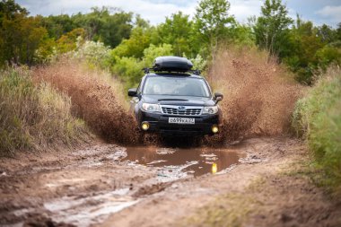 Nikolaevka, Rusya - 23 Haziran 2020: Kara Subaru Forester kirli orman yolunda ilerliyor ve çok fazla su sıçrıyor