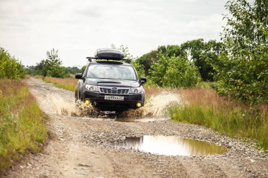 Khabarovsk, Rusya - 26 Haziran 2020: Siyah Subaru Forester çamurlu bir yolda araba kullanıyor. Tekerleklerin altından su fışkırıyor.