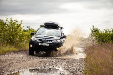 Khabarovsk, Rusya - 26 Haziran 2020: Siyah Subaru Forester çamurlu bir yolda araba kullanıyor. Tekerleklerin altından su fışkırıyor.