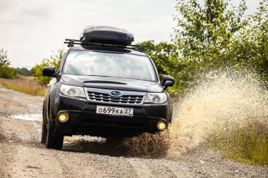Khabarovsk, Rusya - 26 Haziran 2020: Siyah Subaru Forester çamurlu bir yolda araba kullanıyor. Tekerleklerin altından su fışkırıyor.