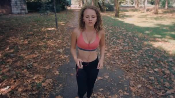 Μια ξανθιά νεαρή γυναίκα τρέχει μέσα από το πάρκο — Αρχείο Βίντεο