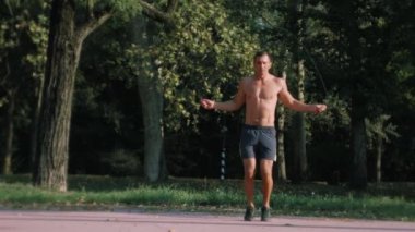 Genç atletik adam açık havada ağır çekimde parkta bir ip atlama ile atlama