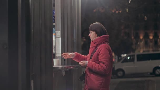 Mujer joven con una taza de té caliente al aire libre en tiempo fresco. Con una chaqueta caliente. Noche calle de la ciudad — Vídeos de Stock