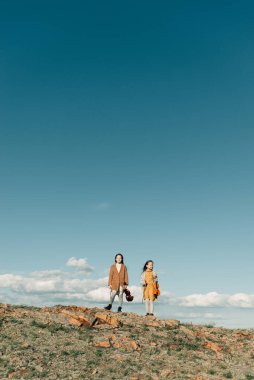 Kemancı iki kız kardeş gün batımında kayalık bir tepede özgürlüklerini hissediyorlar.