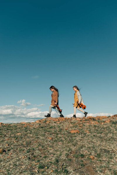 two little girls with violins walking on a rocky hill in the sunset