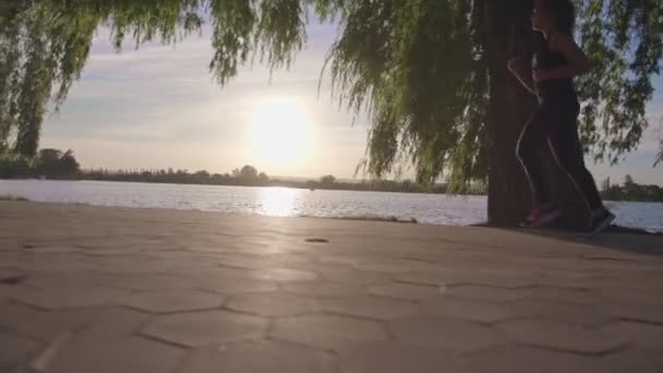 Γυναίκα που τρέχει δίπλα στη λίμνη στο ηλιοβασίλεμα. — Αρχείο Βίντεο