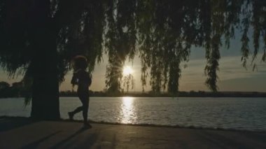 Pratik yoga göl kıyısında günbatımı siluet genç kadın.