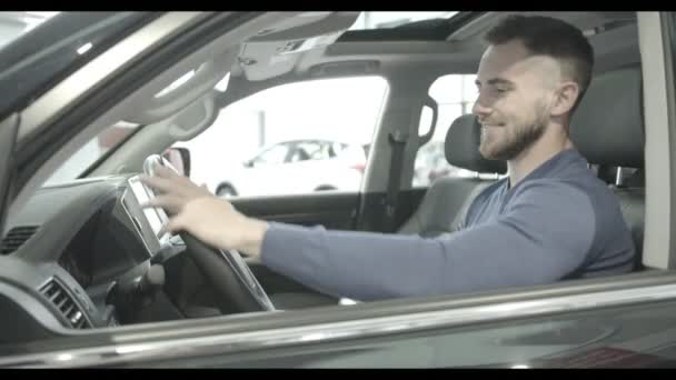 Male Client Enjoying Luxury Car Interior In New Automobile In Auto Salon Smiling Man Keeping Wheel Turning Aside Looking At Camera And Showing Car Alarm System On First Plan Concept Of Buying