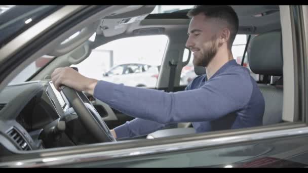 Schöner Mann mit Bart sitzt in gutem Auto und zeigt Schlüssel. — Stockvideo