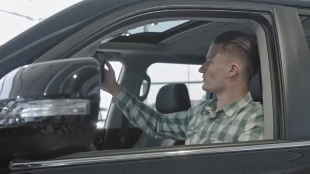 Vista lateral do cliente sentado em carro novo e tomando selfie — Vídeo de Stock