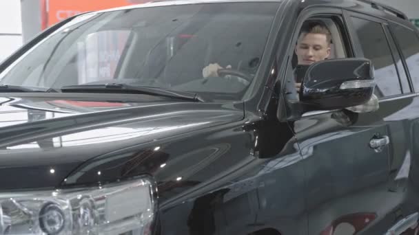 Homem confiante sentado em grande carro preto no salão de auto — Vídeo de Stock