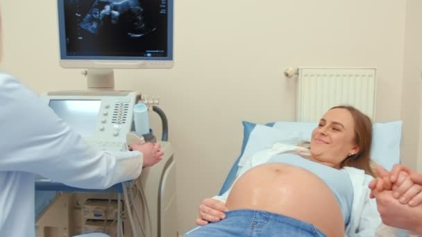 Ein Arzt überträgt ein Foto von Ultraschalluntersuchungen eines glücklichen Paares, sie sehen ein Foto und lächeln — Stockvideo