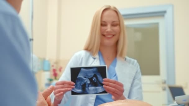 Un medico trasmette una fotografia di ecografia scansione di una coppia felice, guardano foto e sorridono — Video Stock