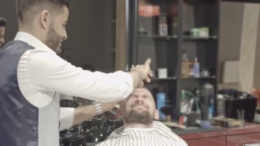 Profesyonel kuaför berber dükkanı sandalyede oturan genç erkek istemci iş parçacığı yordamı ve kaşları düzeltme şeklinde yapmak beyaz gömlekli. Stil oluşturma ve bakımı kavramı.