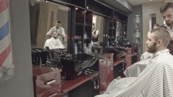 Clientes masculinos legais felizes sentados na cadeira do barbeiro na barbearia hipster interior com iluminação suave do dia . — Vídeo de Stock