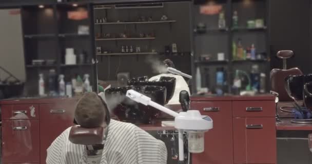 A young man rests in a chair and makes a procedure after shaving. Concept of hairdressing and shave. — Stock Video