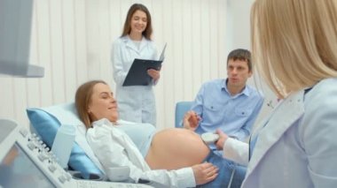 Doktor, hastanede hamile bir kadın için ultrason taraması yapar. Mutlu adam el tarafından karısını tutarak ve ekran izliyor