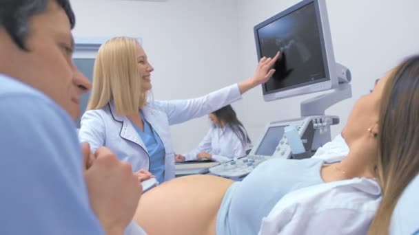 Gravid kvinna och partner tittar på ultraljud genomsökning av barn med läkare. — Stockvideo