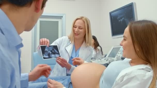 Médecin féminin montrant femme enceinte échographie sur photo expliquant et souriant — Video