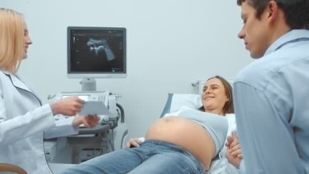 Un marido feliz junto con su esposa para una consulta en la Oficina de Diagnóstico por Ultrasonido. La joven pareja cogida de la mano en la pantalla y sonriendo . — Vídeo de stock