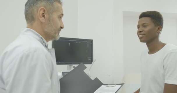 Medico senior parla con il paziente presso l'Ufficio di diagnostica ecografica e fa registrazioni nei quaderni — Video Stock