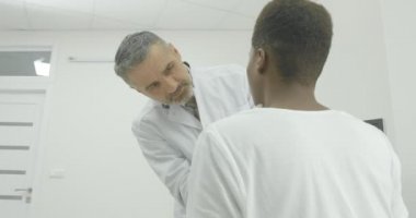 Üst düzey doktor servikal bölgede hastayı inceler. Bir Afrikalı-Amerikalı bir kanepede oturur ve bir uzman sonucu bekliyor.