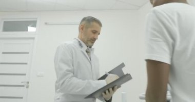 Kıdemli Doktor Genç hastayı önerir. Bir doktor hasta ile konuşur ve bir dergiye kayıt yapar
